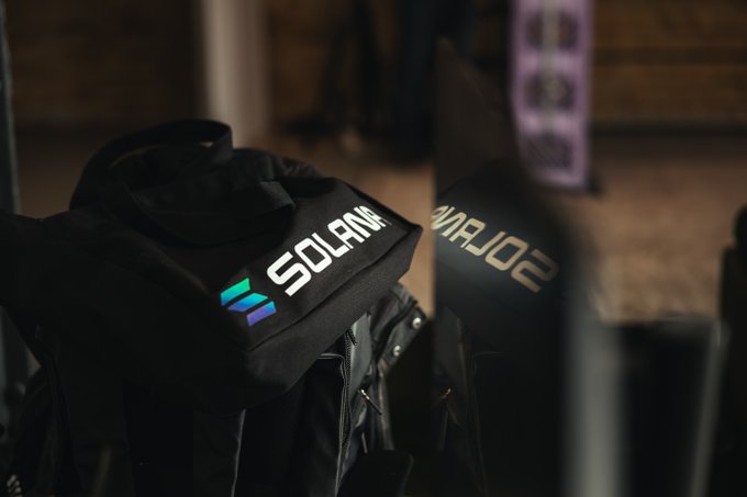 A black backpack or jacket features a white 'SOLANA' logo with the colorful Solana emblem, photographed against a dark background with its reflection visible.