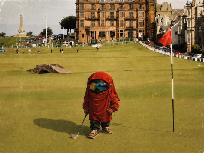 A small figure wearing a red hooded cloak and reflective sunglasses stands on a golf green holding a club, with a historic stone building and red flag in the background.