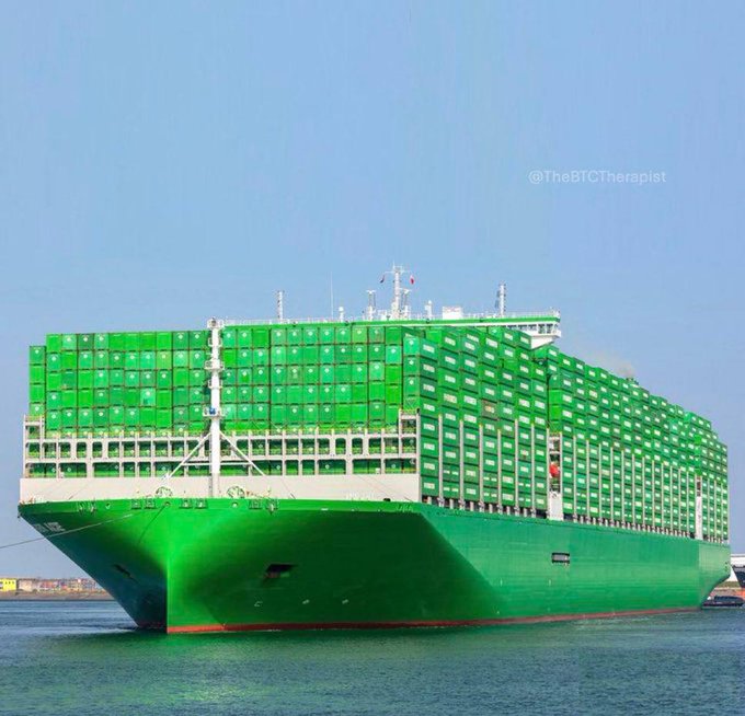 A large green container ship loaded with green shipping containers floats on water under a clear sky, watermarked with '@TheBCTherapist'.