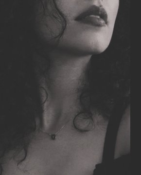 A close-up black and white portrait focusing on a woman's lips, neck, and collarbone area, wearing a delicate pendant necklace.