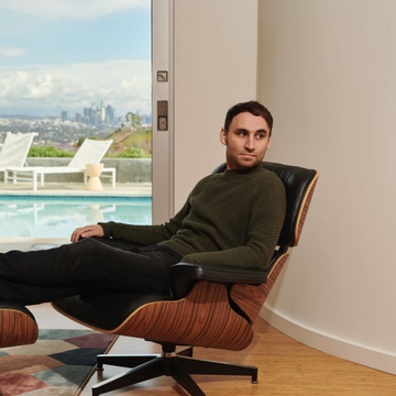 A man in a dark green turtleneck reclines in a mid-century modern lounge chair beside a floor-to-ceiling window overlooking a pool, patio chairs, and a city skyline with a tall tower in the distance. The relaxed, contemplative pose paired with the "Bottom signal" caption suggests Nikita Bier is signaling a contrarian buy opportunity, with "Send everything to ATHs" implying an expected rally to all-time highs.