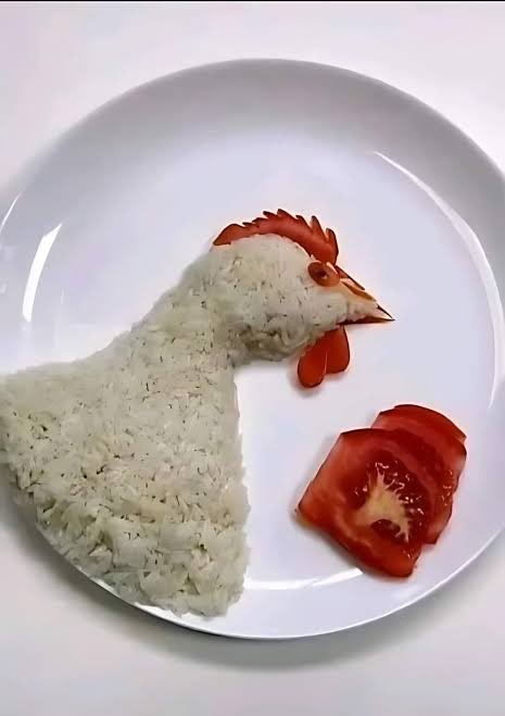 A white plate features a creative culinary arrangement where white rice is shaped into the silhouette of a chicken or rooster, accented with sliced tomato pieces for the comb, wattle, and beak, accompanied by tomato wedge slices. The playful food art cleverly mirrors the post's message about sacrificing now (investing in XRP) to enjoy life's simple pleasures later—like a hearty meal—with greater appreciation.