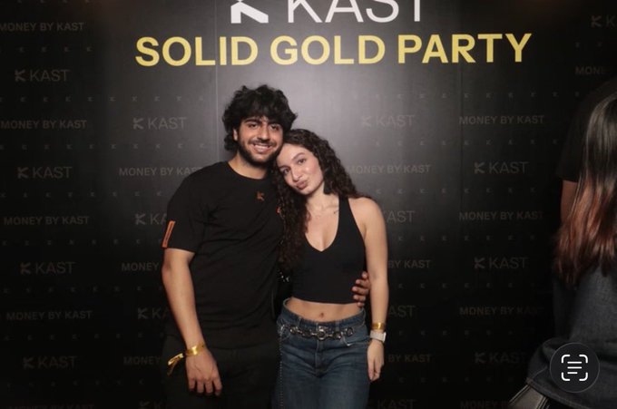 A couple poses together at the 'KAST SOLID GOLD PARTY' in front of a branded backdrop reading 'MONEY BY KAST'.