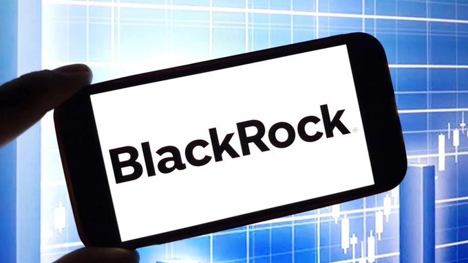 A hand holds a smartphone displaying the "BlackRock" logo on a white screen, set against a blue background featuring candlestick chart patterns. The image visually ties into the post's theme of BlackRock's shifting on-chain Bitcoin activity becoming increasingly difficult to interpret for traders monitoring ETF flows.