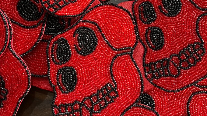 A close-up of beaded artwork featuring red skulls with black detailing, appearing to be made of intricate beadwork.