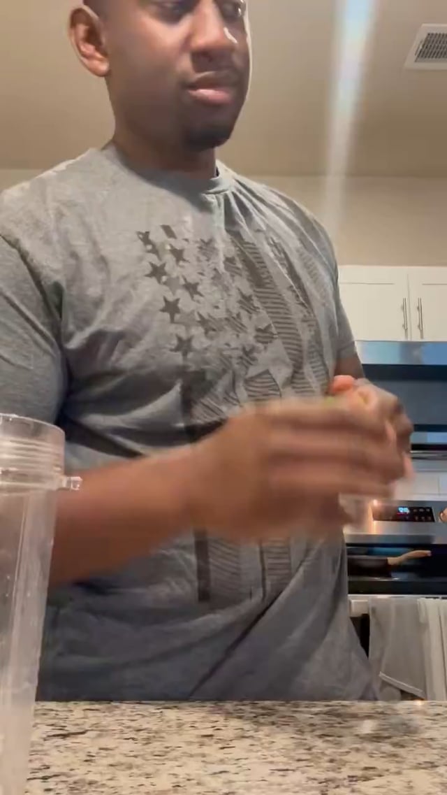 A man wearing a gray graphic t-shirt with a star design stands in a kitchen, holding what appears to be a cup while looking downward. The image shows a casual domestic scene but contains no visible text, numbers, or identifiable logos related to "SPX6900" mentioned in the post, suggesting the image is unrelated to the cryptocurrency content referenced.