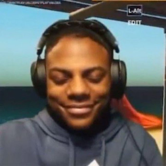 Screenshot of a man wearing headphones with eyes closed, smiling slightly, appearing to be on a video call with ocean view in background.