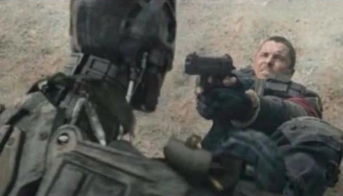 A scene from a sci-fi/action film showing a character in tactical gear aiming a pistol while grappling with another armored figure wearing a skull-like mask.