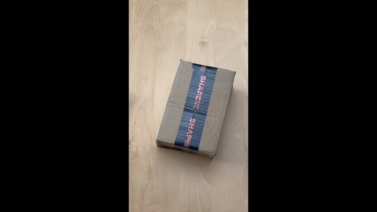The image shows a brown cardboard box that has been cut open, revealing its contents inside. The box appears to be a wallet or money management tool designed for Bitcoin and Ethereum transactions. It features a red stripe along with the text "Can your hardware wallet do this? May look gimmicky, but this shows @Keycard_ is the most modular, open-source, & secure wallet imho for BTC & ETH". The box has been opened on a wooden surface, possibly indicating that it was recently used or is being displayed.