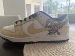 A pair of Nike sneakers featuring a colorful winged design and a Nike Swoosh logo sits on a white rug near a bright window, showcasing the unique footwear referenced as the "coolest shoes in web3." The image highlights the distinctive cream-colored sneakers with their eye-catching angel wing artwork, aligning with the boast about owning standout shoes in the web3 community.