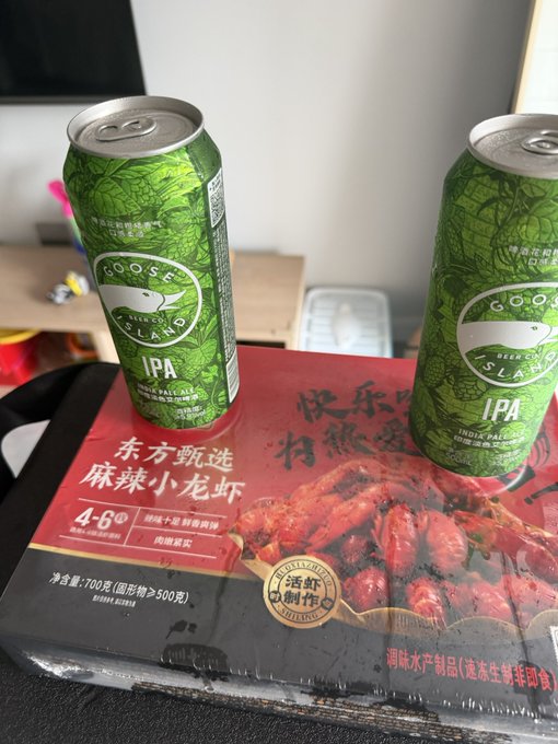 Two cans of Goose Island IPA beer sit on top of a red package of spicy crayfish (麻辣小龙虾) labeled with Chinese text including '4-6 分钟'.