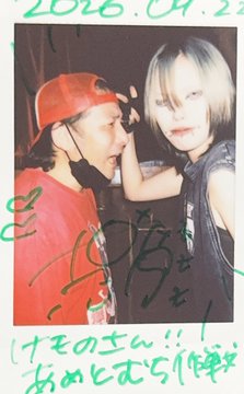A vintage-looking signed polaroid photo dated "2016.04.2" featuring two young people, one in a red cap and the other with blonde hair, with Japanese writing and signatures across it.
