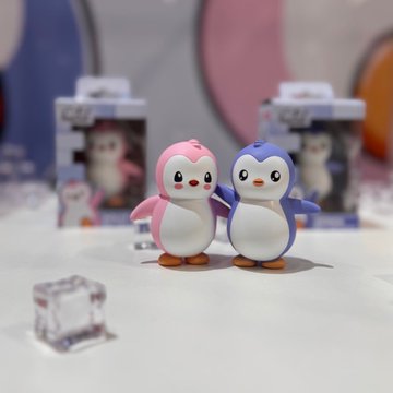 Two small penguin figurines, one pink and one blue, displayed with their original packaging in the background.