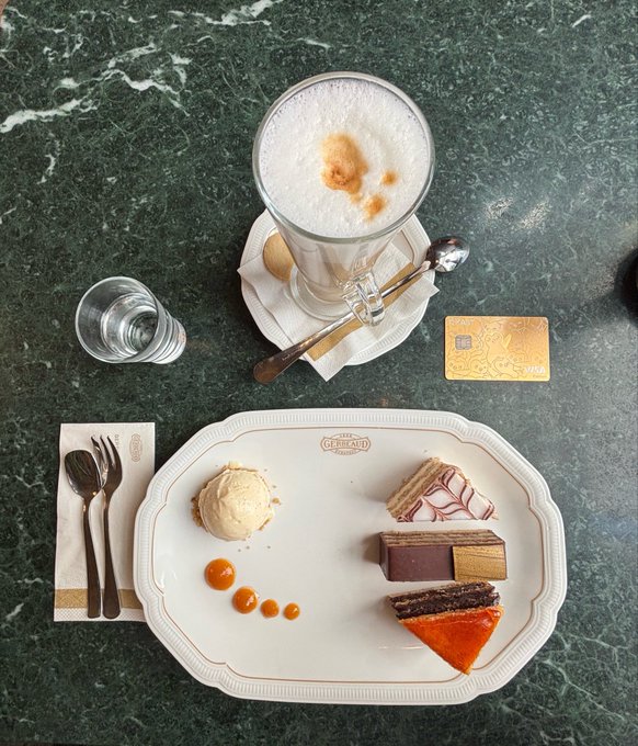 A dessert plate from Gerbeaud displays assorted pastries and ice cream alongside a latte and a small glass of water.