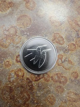 A close-up photo of a metallic coin or medallion bearing the Spider-Man logo resting on a speckled, marbled countertop.