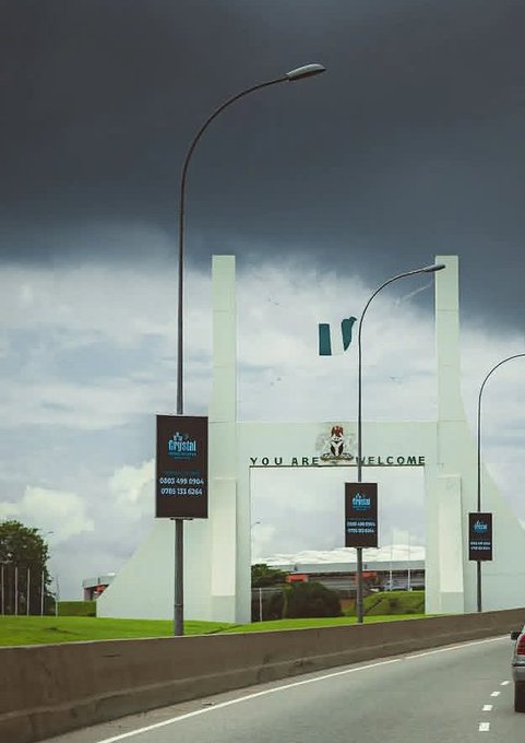 The image shows a white archway with a sign that says "you are welcome" above an entrance, possibly at a border crossing or a public building. There are three signs posted outside of this structure, one of which reads "you are welcome". A car is driving by in front of the archway, and there's a cloudy sky overhead. The image also contains text that says "you are welcome" and "you are welcome", as well as other phrases related to security and privacy concerns.