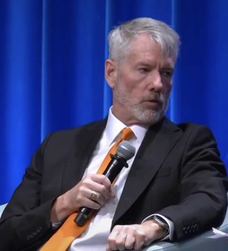 Michael Saylor, executive chairman of MicroStrategy, speaks into a microphone while wearing a dark suit and an orange tie, seated against a blue curtain backdrop during a fireside chat.

The image illustrates the post's reference to Saylor's appearance at DC Fintech Week, where he discussed Bitcoin tailwinds for $MSTR during a conversation with Chris Brummer at the World Bank.