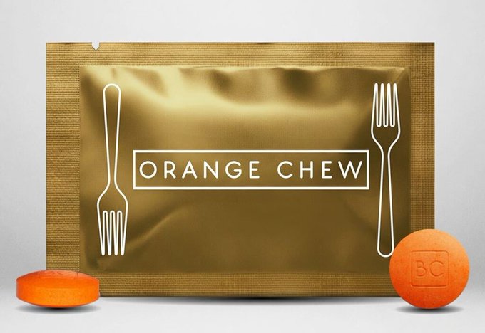 A gold "ORANGE CHEW" food pouch featuring fork graphics on either side, displayed with orange disc-shaped candies.