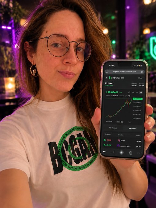 A smiling woman with glasses holds up her smartphone displaying a cryptocurrency chart for BC Token, showing a price of $0.03467 and a positive upward trend.