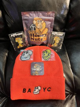 A flat lay on a dark leather surface showing Honey Nuts branded merchandise including an orange 'BABYC' beanie with Nuggie patch, snack packaging, and additional Nugget patches.