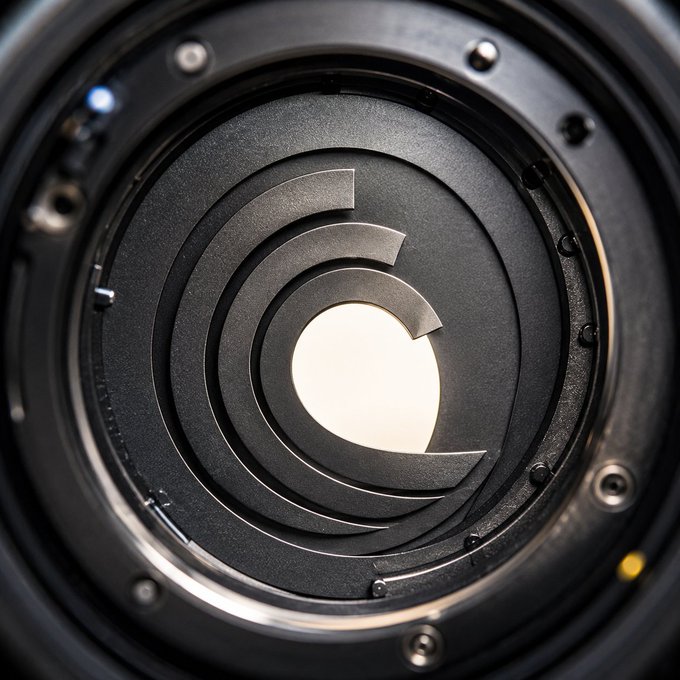 The image shows a close-up of a camera lens featuring an aperture diaphragm with a "C" logo at its center, which aligns with the post's "GM" reference to Glassroom and the "Quarter century, endless reach" tagline symbolizing 25 years of vision and expanding influence.