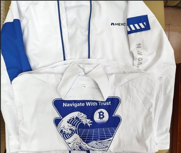 White and blue clothing items are displayed, featuring 'MEXC' branding and 'Navigate With Trust!' printed around a Bitcoin logo.