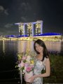 A woman in a white dress with "Happy" written on the sleeve poses with a bouquet in front of Marina Bay Sands in Singapore. The caption introduces her as Steff, based in SG, highlighting her new life in the city and her transition into crypto.