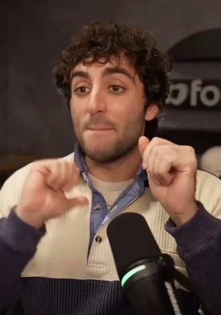 A curly-haired man gestures emphatically with both hands raised while speaking into a microphone, appearing on what looks like a podcast or interview show. The image visually captures the enthusiastic, animated delivery referenced in the post about a trader hyping up his $STONK position as his "best trade ever" and "biblical."