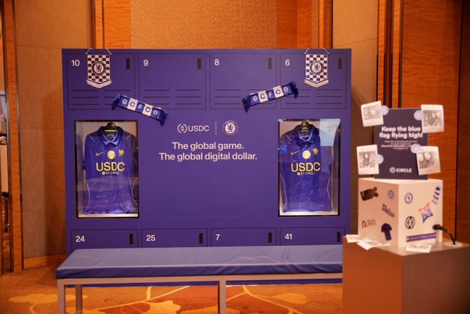 An indoor display featuring two framed purple Chelsea FC "USDC" jerseys in locker-style frames with numbers 10, 9, 8, and 6, alongside text reading "The global game. The global digital dollar."