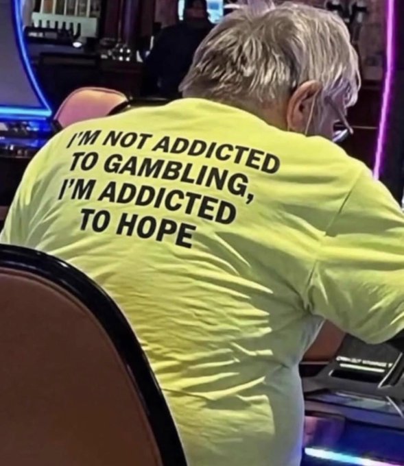 A person with blonde hair sits in a casino chair wearing a yellow shirt that reads "I'M NOT ADDICTED TO GAMBLING, I'M ADDICTED TO HOPE." The image humorously captures the post's message that crypto trading is less about strategy and more about chasing hope for the next big win.