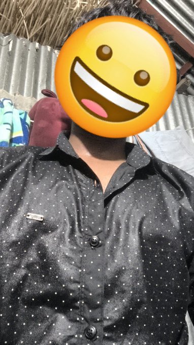 A person wearing a black shirt with small white polka dots, with their face completely covered by a large, smiling yellow emoji graphic.