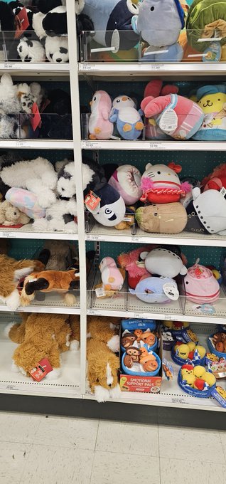 A store shelf display filled with various plush toys and Squishmallows, including pandas, foxes, and other characters, alongside packages of 'Squishmallows' dog toys.
