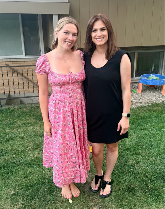 Two women smile together outdoors on a grassy lawn, with one wearing a pink floral dress and the other in a black sleeveless dress, while a child's blue water table is visible in the background. The casual backyard setting and relaxed poses reinforce the post's playful suggestion that widespread crypto adoption feels close at hand.