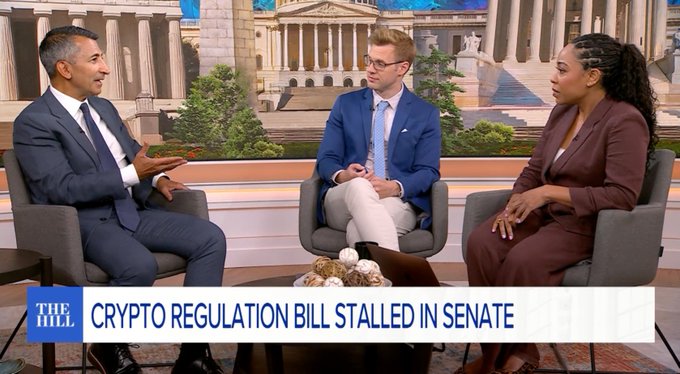 Three people sit in armchairs on a TV studio set with a capitol building backdrop, engaged in discussion. The on-screen graphic reads "THE HILL CRYPTO REGULATION BILL STALLED IN SENATE," fitting the post about discussing the CLARITY Act on Rising with The Hill alongside hosts Lindsey and Robby.