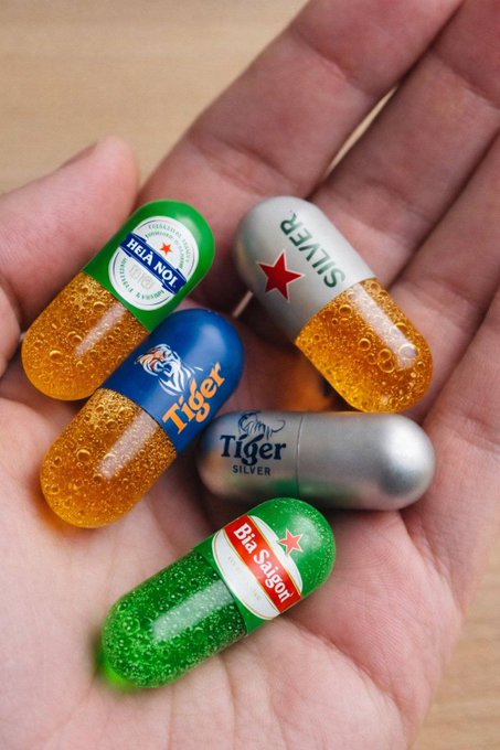The image features a person's hand holding five different colored pills, each with a label that says "Tiger" or "Silver", along with the names of various brands such as "Hollasn", "Bia Sáng", "ETH", and "BTC". The person is holding these pills in their hand, showcasing them off to the viewer.