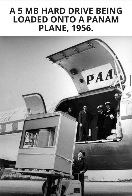 A black-and-white historical photograph with the caption 'A 5 MB HARD DRIVE BEING LOADED ONTO A PANAM PLANE, 1956,' showing men loading equipment into a Pan Am aircraft.