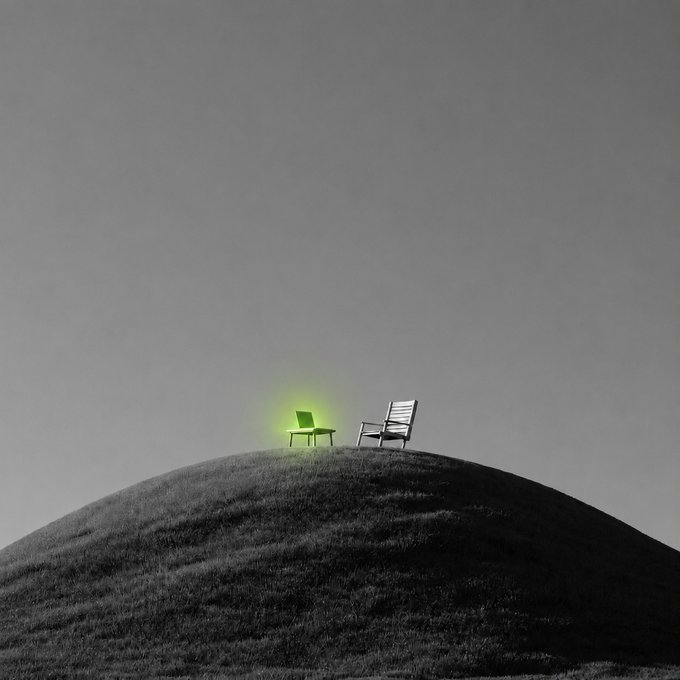 Two chairs sit atop a grassy hill against a gray sky, with one chair glowing bright green like a laptop screen, creating a striking contrast that suggests someone left their computer open in the peaceful outdoor setup.