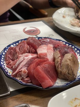 A photograph of a plate containing various cuts of raw meat including red meat slices and what appears to be organ meat, set on a restaurant table.