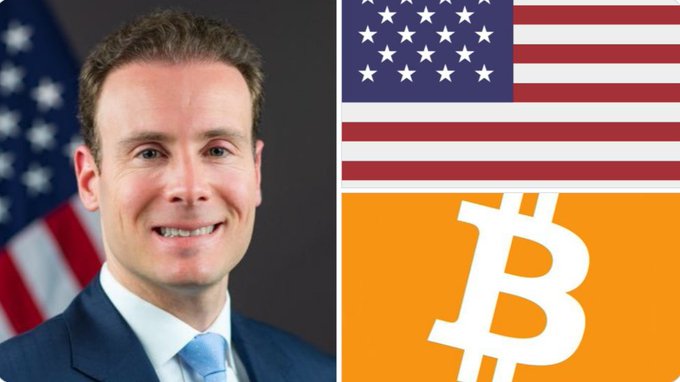 A man in a dark suit and blue tie smiles in front of an American flag, positioned alongside the U.S. flag and Bitcoin logo. The image aligns with CFTC Chairman Mike Selig's push for the Clarity Act, symbolizing the intersection of U.S. policy and cryptocurrency regulation.