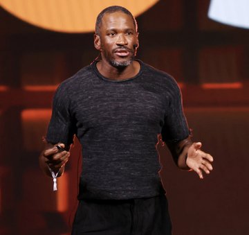 Arthur Hayes, the BitMEX co-founder, is shown speaking on stage in a dark sweater, gesturing with his hands during a presentation. The image relates to the post by depicting the prominent crypto figure behind recent Ethereum purchases, where he has accumulated 7,213 ETH since July 15 despite facing approximately $301,000 in unrealized losses.