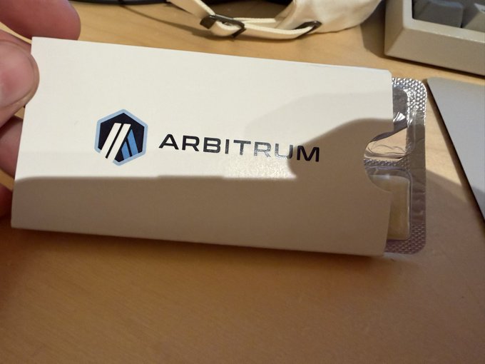 A hand holding a white product box branded with the 'ARBITRUM' logo and name, featuring a blister pack of pills visible inside.