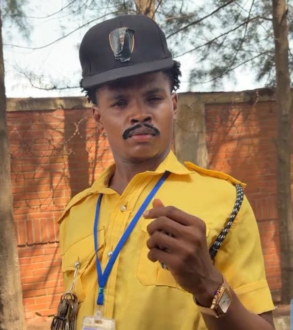 A man dressed in a yellow security guard uniform with a cap and lanyard stands in front of a brick wall, pointing his finger forward. The image humorously suggests that the security guard should be hired by "Stake," playing on the post's joke about needing better protection or staff.