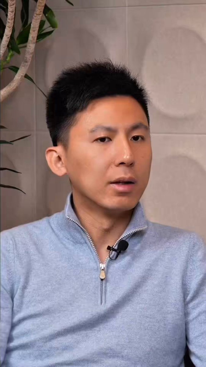 The image features a man wearing a blue sweater, sitting down with his head tilted slightly to one side as he looks off into the distance. The background of the photo shows a wall with a plant behind him, adding some greenery to the scene. The caption for this image reads "He was at Huobi when it was the largest exchange in crypto, before Binance even existed Invested in Circle before stablecoins were even a conversation and helped govern USDC from the ground up Early conviction like this is rare @aptAlix @Aptos Ft. @davidgan1818".