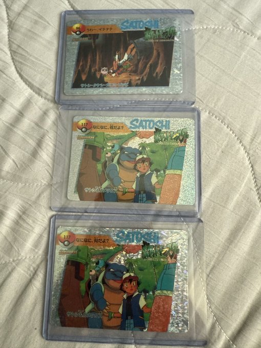 Three Japanese Pokémon trading cards in protective sleeves, each labeled 'SATOuji' and numbered 110, 111, and 117, lying on a white quilted surface.