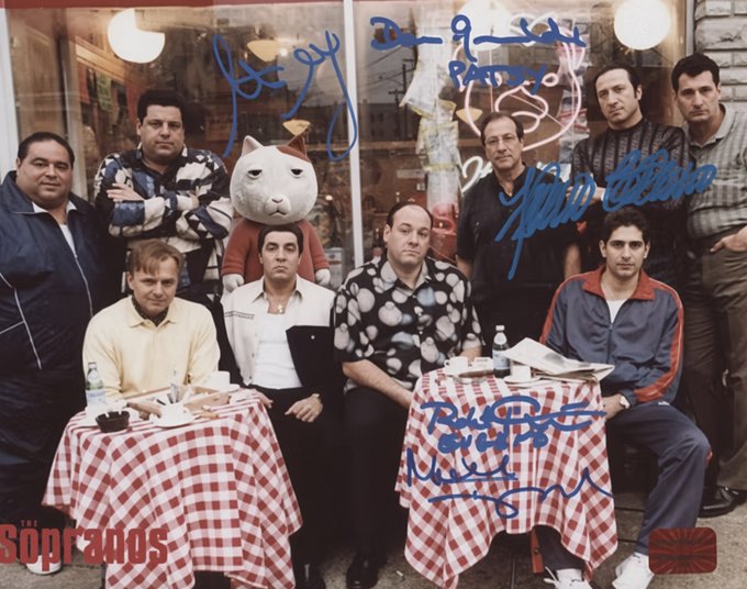 A signed cast photo from 'The Sopranos' showing the cast members seated at a restaurant with red-checkered tablecloths, with multiple autographs in blue marker across the image.
