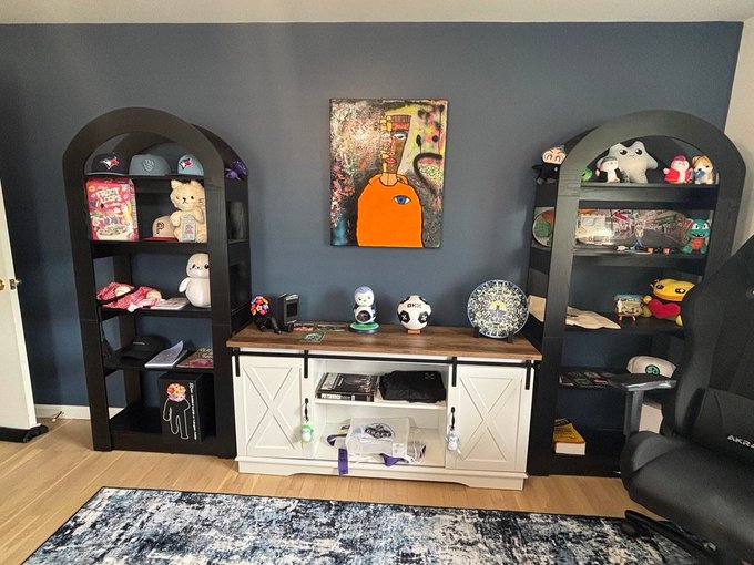 A dark navy gaming office setup features two arched black bookshelves flanking a white sliding-door cabinet, decorated with plush toys, Funko Pops, and crypto-themed art including a Manic-style painting, an OKX-branded soccer ball, and a Sony PlayStation soccer ball. The arrangement ties into the post's "Web3 office" theme, showcasing the freshly added OKX ball alongside other gaming and NFT-inspired decor.