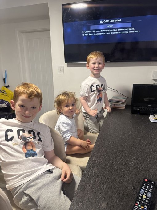 Three young children sit in front of a wall-mounted TV displaying 'No Cable Connected' and an HDMI2 source selection screen.