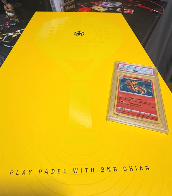 A bright yellow padel court features the text “PLAY PADEL WITH BNB CHIAN,” with a protected Pokémon card placed near the sideline.
