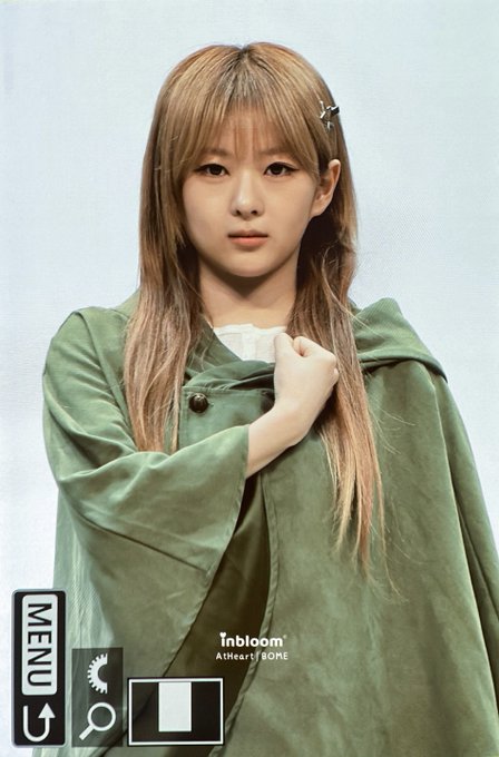 A portrait photo of a young woman with long blonde hair wearing an olive-green cloak, with text reading "inbloom A'theart of BONE" and a "MENU" UI element visible.