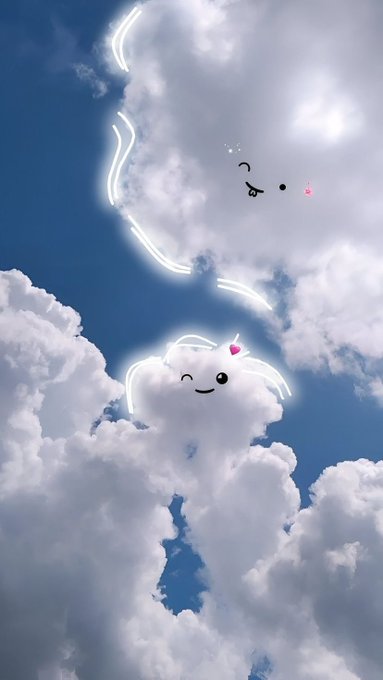 A whimsical photograph of fluffy white clouds against a blue sky, with cartoon face and bunny-ear doodles drawn on two cloud formations using a glowing white line effect.